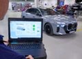 A technician uses a laptop with diagnostic software to monitor a BMW i7 sedan inside a brightly lit automotive workshop, highlighting advancements like all-solid-state EV batteries.