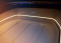 Close-up view of a luxury BMW V8 Shooting Brake trunk space with beige leather lining, accent lighting, and a branded metal emblem on the rear panel.