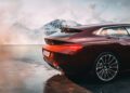 A maroon BMW Speedtop sports car is parked on a reflective surface with snow-covered mountains and a cloudy sky in the background.