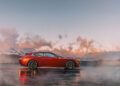 A red BMW Shooting Brake is parked on a wet surface with mountains and a cloudy sky in the background at sunset.