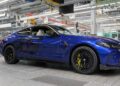 A blue BMW M4 CS with black wheels and yellow brake calipers is parked on the floor of an automotive factory assembly line, exuding a sense of luxury.