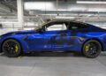 A blue BMW M4 CS sports coupe with black wheels and yellow brake calipers, styled as a VR46 edition, is parked inside a modern industrial garage, showcasing bespoke luxury details.