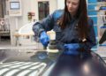 A woman wearing work gloves and overalls uses a power tool to polish a large metal surface in an industrial workshop, giving it the care and precision you'd expect for a luxury finish.