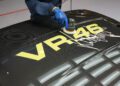 A person uses a polishing tool on a black car hood featuring the yellow text "VR46" and a large white signature decal, highlighting the bespoke luxury of this VR46 edition.