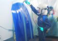 Person in protective gear spray-painting a large BMW M4 CS hood in a workshop, crafting a bespoke luxury finish.