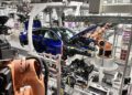 Robotic arms assemble blue BMW M4 CS cars on an automated production line inside a modern automotive manufacturing facility, showcasing bespoke luxury and advanced engineering.