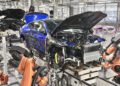 A blue luxury car is being assembled by robotic arms on an automotive production line inside a modern factory.