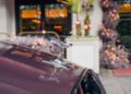 Close-up of a silver Rolls-Royce “Spirit of Ecstasy” hood ornament on a burgundy car, with Chelsea London’s floral and architectural backdrop softly blurred in the background.