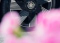 Close-up of a Rolls-Royce Spectre wheel with black and silver spokes, partially obscured by out-of-focus pink flowers in the foreground, captured in Chelsea London.