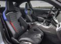 The image shows the interior of the 2026 BMW M2 CS sports car with two black leather racing seats, carbon fiber accents, and a modern dashboard with a digital display, all hinting at its impressive 523HP performance.