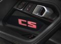 Close-up of a BMW M2 CS car door interior, showcasing control buttons, a metallic handle, and illuminated red "CS" text on a carbon fiber panel—highlighting the sporty details of the 523HP 2026 BMW.