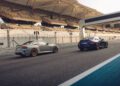 BMW unveils the 523HP 2026 M2 CS as two sports cars are parked side by side on a race track in front of empty grandstands under a covered structure.