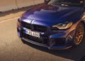 A close-up view of the front of a blue BMW 2026 M2 CS parked on a sunlit road, showcasing its grille, headlights, front bumper, and license plate—hinting at the power of its 523HP engine.