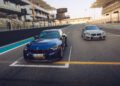 Two BMW sports cars, including the 523HP BMW 2026 M2 CS, are parked side by side on a race track near the starting line with empty grandstands in the background.