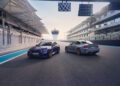 Two sports cars, including the BMW 2026 M2 CS boasting 523HP, are parked side by side on a race track near the finish line, with grandstands and a tower visible in the background.