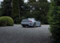 A gray BMW M2 CS sports car is parked on a gravel driveway surrounded by green trees and bushes.