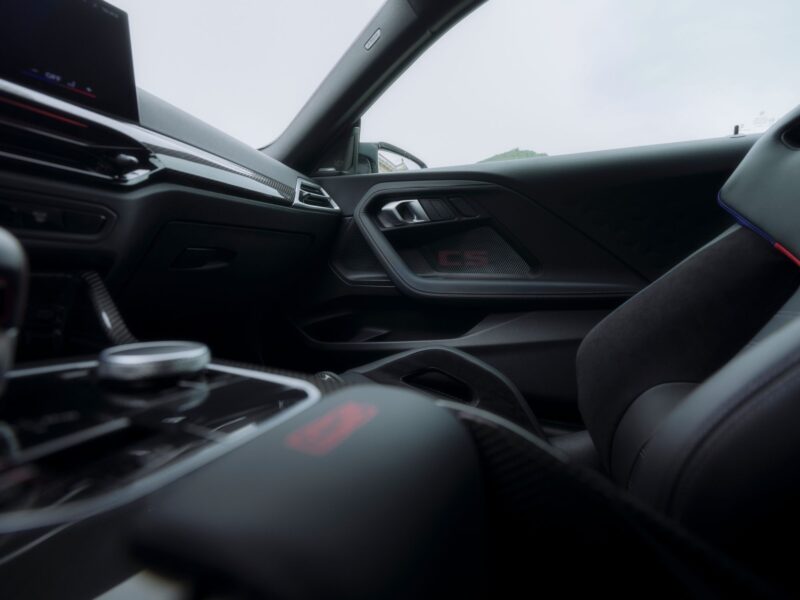 Interior of a modern car showing the dashboard, center console, and passenger seat, with "CS" visible on the passenger door panel—capturing the refined sportiness of the BMW M2 CS.