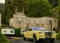 A yellow Rolls-Royce Phantom sedan is displayed on a platform in front of the ornate Villa d'Este, its arches and detailed stonework evoking scenes from Goldfinger, surrounded by lush greenery.