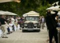 A classic black Rolls-Royce Phantom glides through an outdoor event at Villa d'Este, passing seated attendees amid umbrellas and lush greenery.