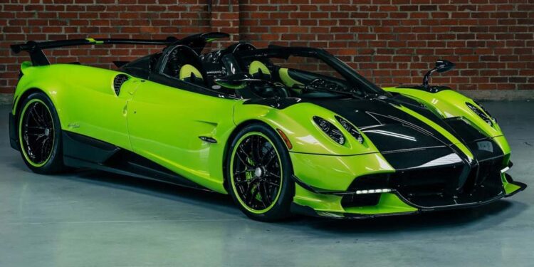 A bright green and black Pagani hypercar is parked indoors in front of a brick wall and large windows.