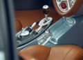 Close-up of a luxury car interior, reminiscent of Pagani hypercars, featuring brown leather seats with a checkered pattern and a metallic gear shifter on the center console.