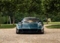 A blue Huayra Epitome luxury sports car is parked on a cobblestone path at Villa d'Este, surrounded by green grass and trees.