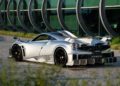 A silver Pagani Huayra Epitome hypercar is parked on a stone-paved surface in front of a modern glass building with circular window frames, evoking the elegance of Villa d'Este.