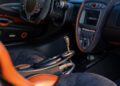 Interior of a luxury sports car with leather and carbon fiber accents, inspired by Imola, featuring a central touchscreen, distinctive gearshift, and sporty steering wheel.