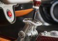 Close-up view of a luxury car interior, featuring a gated manual gear shifter with a red and white knob, leather and metal accents, and a red engine start button—evoking the craftsmanship found in Pagani hypercars.