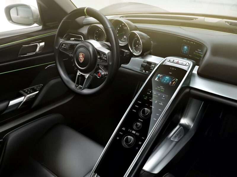 Close-up view of a Porsche car interior showing the steering wheel, digital instrument cluster, and central touchscreen—highlighting modern controls and displays found in both the Porsche Carrera GT and Porsche 918 Spyder for an informed comparison.