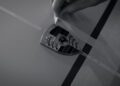 A hand places masking tape next to a Porsche logo badge on a flat, smooth surface—hinting at the meticulous care often given to exotic models like the 918 Spyder.