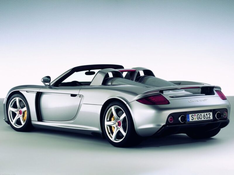 A silver convertible sports car, reminiscent of the Comparison: Porsche Carrera GT Vs Porsche 918 Spyder, is parked in a studio setting and shown from the rear three-quarter angle.