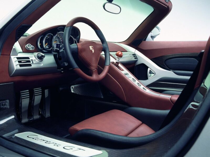 Interior view of a Porsche Carrera GT showing the steering wheel, dashboard, gear shifter, and red leather seats with metallic and carbon fiber trim—highlighting the craftsmanship in the Comparison: Porsche Carrera GT Vs Porsche 918 Spyder.