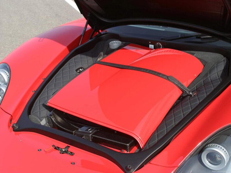 The front trunk of a red sports car, open to reveal a matching red removable roof panel stored inside—a feature showcased in many automotive reviews, including those comparing the Porsche Carrera GT vs Porsche 918 Spyder.
