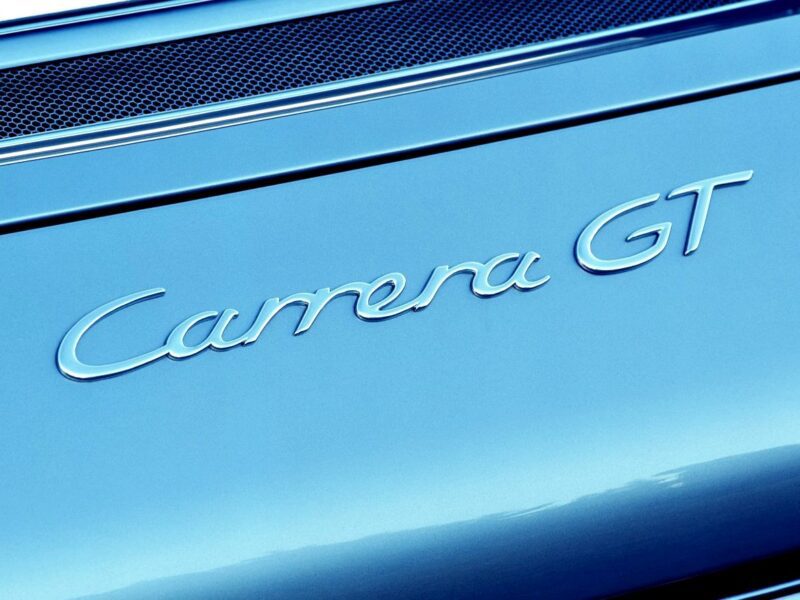 Close-up of the "Carrera GT" badge on a blue car, with a mesh grille visible in the background—perfect for enthusiasts interested in a Comparison: Porsche Carrera GT Vs Porsche 918 Spyder.