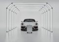A white sports car is parked inside a minimalistic light tunnel, with a Porsche Design Roadster Aluminum Luggage suitcase in matching white positioned in front—an exquisite scene that inspires you to buy your next travel essential.