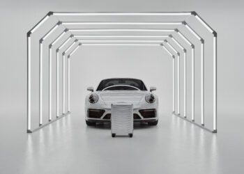 A white sports car is parked inside a minimalistic light tunnel, with a Porsche Design Roadster Aluminum Luggage suitcase in matching white positioned in front—an exquisite scene that inspires you to buy your next travel essential.