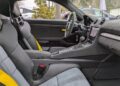 Interior of a modern Porsche 718 Cayman GT4 RS featuring black and gray seats with yellow seat belts, center console, touchscreen display, and a steering wheel—part of the exclusive Weissach Package.