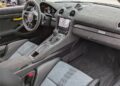 Interior of a modern Porsche 718 Cayman GT4 RS featuring black and grey seats, manual gearshift, touchscreen display with navigation, and suede-like dashboard material—all enhanced by the exclusive Weissach Package.