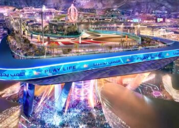 A large elevated race track labeled "PLAY LIFE" overlooks a brightly lit cityscape, with crowds gathered below and colorful lights illuminating the area—this upcoming F1 track’s opening corner is 20 storeys up in the sky.