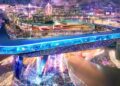 A futuristic, elevated sports arena with a racetrack—whose opening corner is 20 storeys up in the sky—glows with neon lighting and “PLAY LIFE” in English and Arabic, overlooking a crowded, brightly lit urban area at night.