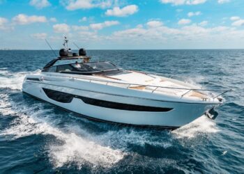 A sleek, modern luxury yacht cruises on open water under a partly cloudy sky, creating white waves behind it—a true maritime experience.