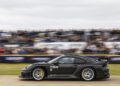 A black sports car speeds past spectators on a track, with motion blur emphasizing its movement.
