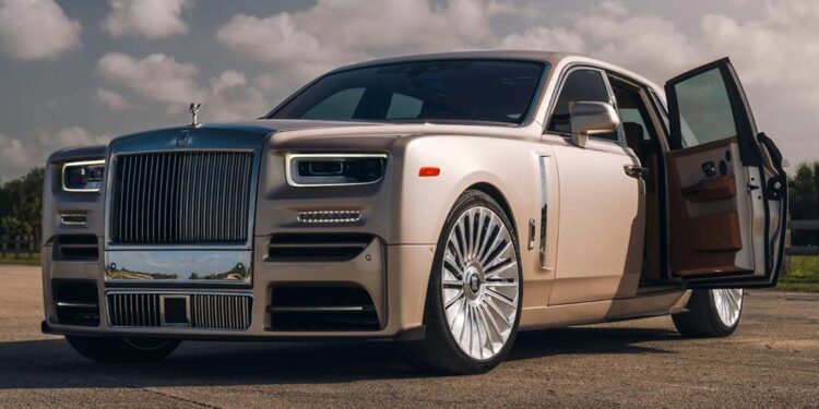 A beige Rolls-Royce sedan, one of the most expensive luxury cars of all time, is parked outdoors on pavement with its front passenger door open under a partly cloudy sky.