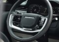Close-up of a modern Range Rover SV Carmel Edition’s steering wheel and dashboard, showcasing digital displays and control buttons—highlighting the luxury found in exclusive Rovers for sale.