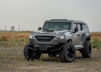 A matte gray armored SUV with large off-road tires, a true unique garage creation, is parked on rough, grassy terrain under an overcast sky.