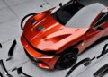 A red Ferrari sports car is parked on a gray concrete surface, enhanced by RNG Design's limited-run body kit, with black car parts and trim pieces floating around it for a bespoke makeover.