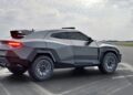A matte gray angular SUV with off-road tires, inspired by apocalypse-ready design, is parked on an empty paved surface under a partly cloudy sky—here’s what makes the Rezvani Knight an apocalypse-ready Lamborghini Urus.