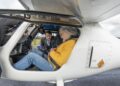 Two people sit inside the cockpit of a small white aircraft, while another stands outside inspecting equipment—capturing the anticipation of An Emotional Homecoming: James May and Richard Hammond Race to the Top Gear Track in EVs.