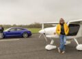 An emotional homecoming: James May leans against a white airplane while Richard Hammond stands by a blue car holding a wheel on an airstrip under overcast skies, as they race to the Top Gear track in EVs.